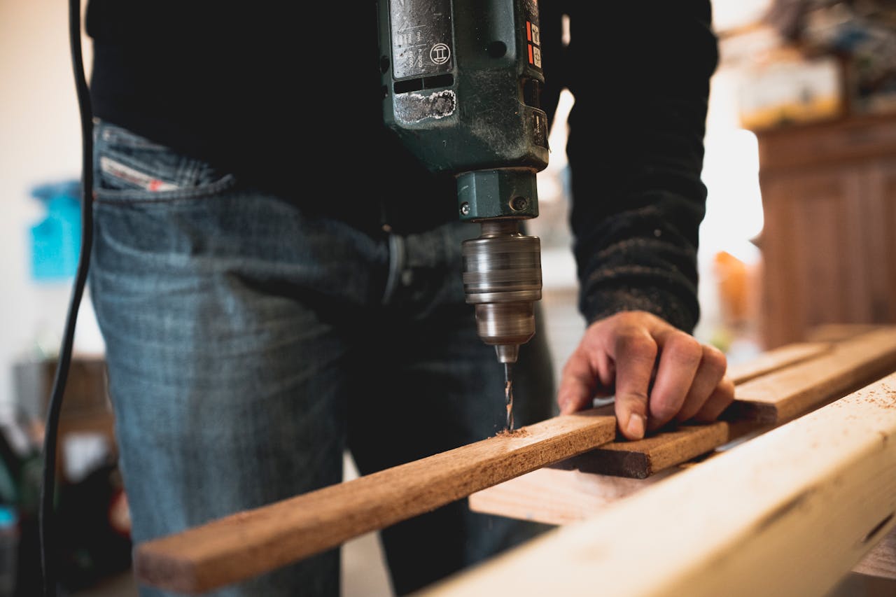 our-experience Close-up of a person using an electric drill on a wooden plank, showcasing detailed woodworking skills.