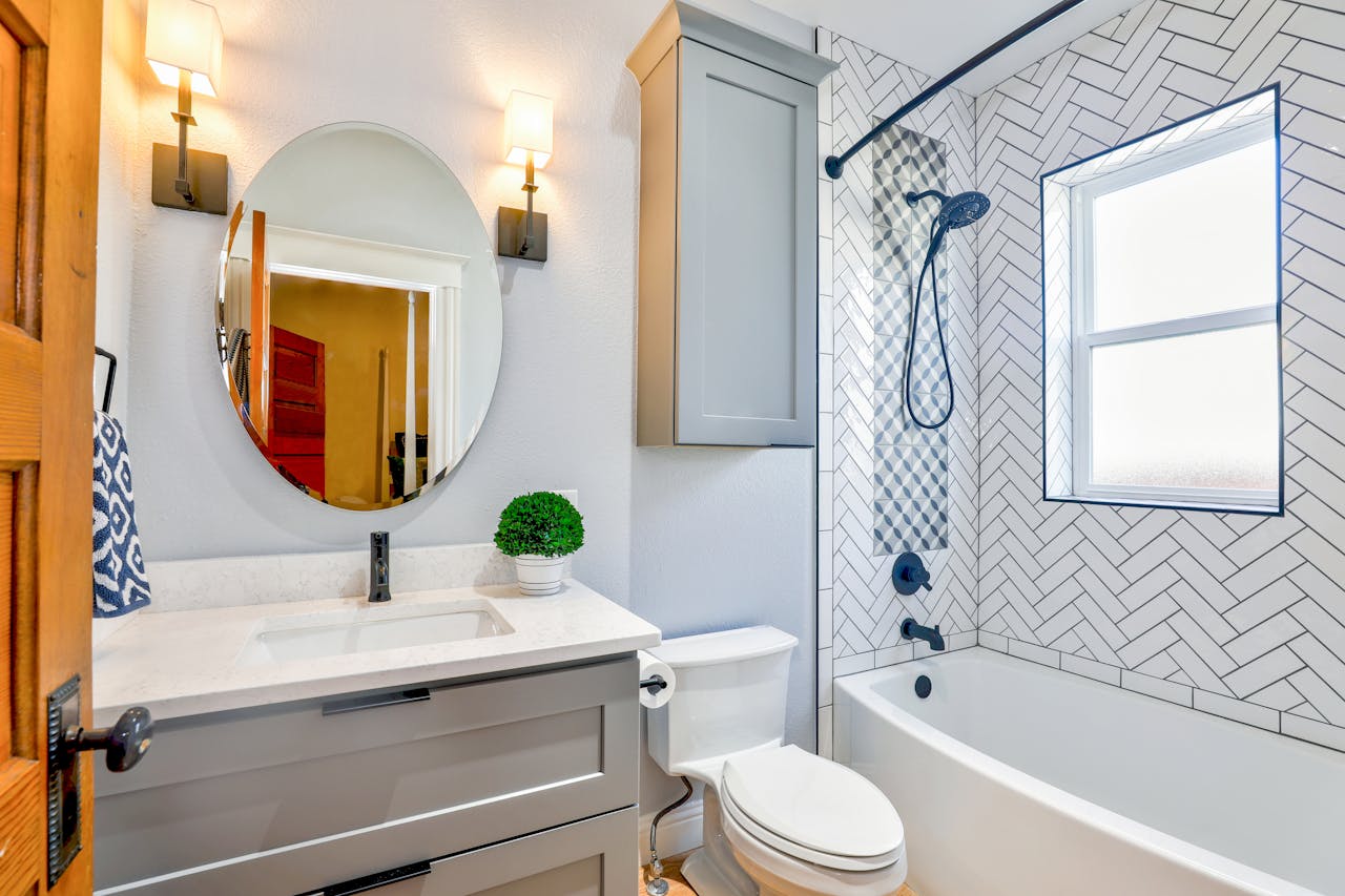 contact-img Elegant modern bathroom featuring chevron tiles, oval mirror, and sleek fixtures for a contemporary look.