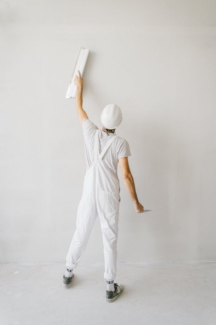 gallery-4 Back view of construction worker in overalls painting a wall white.