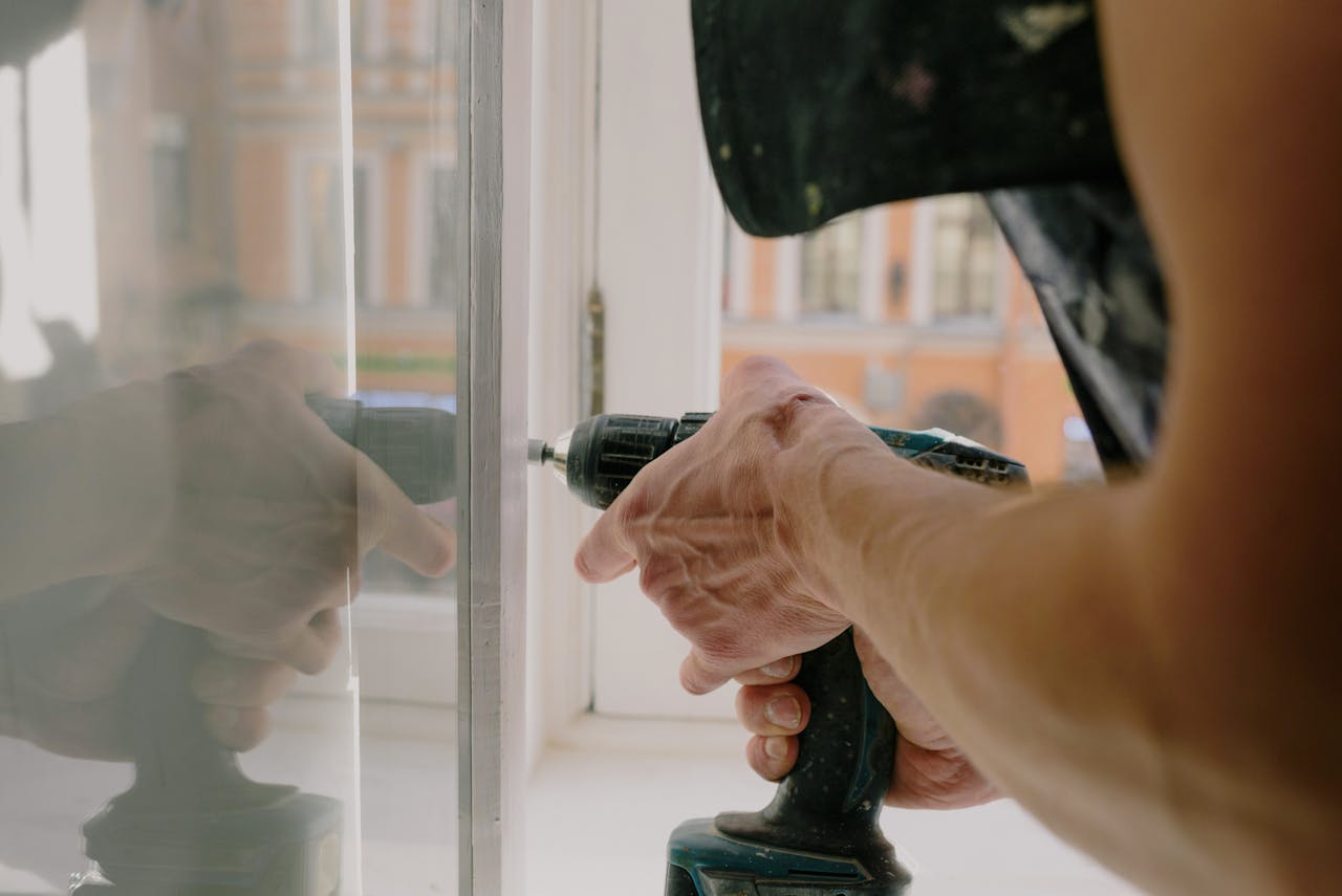 about-02 Close-up of a handyman's hands using a drill to fix a window inside an apartment.