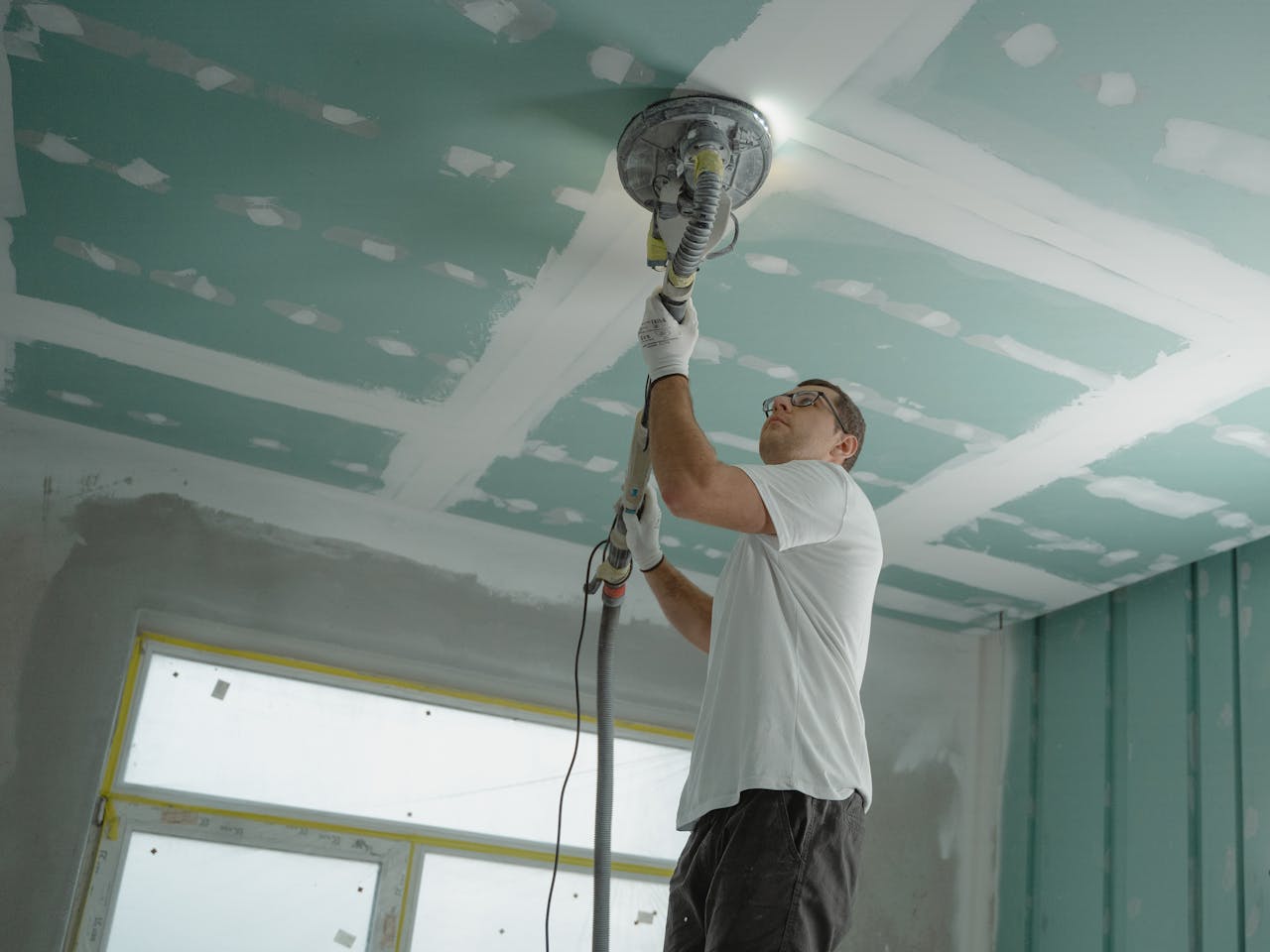 ours-journey A professional worker sanding the ceiling during a home renovation project. Indoor construction setting.