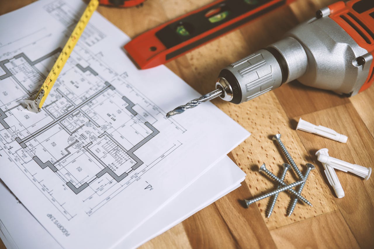 services-img Close-up of construction blueprint with tools like drill and screws on a wooden table.